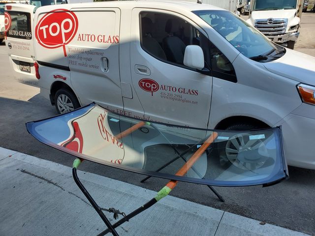 New windshield on a stand beside a white Top Auto Glass van