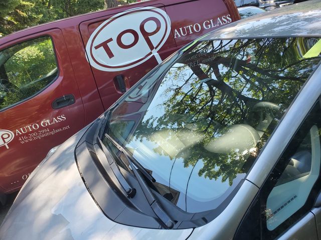 Car with a freshly installed windshield parked beside a red Top Auto Glass van